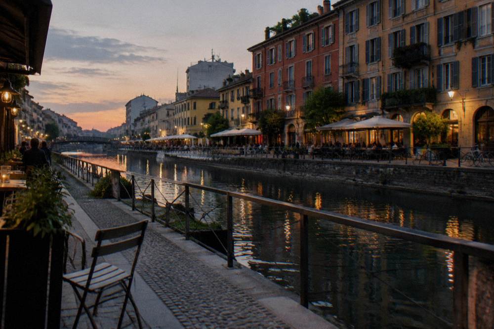 An outdoor table with beer glasses beside a Milan canal at dusk