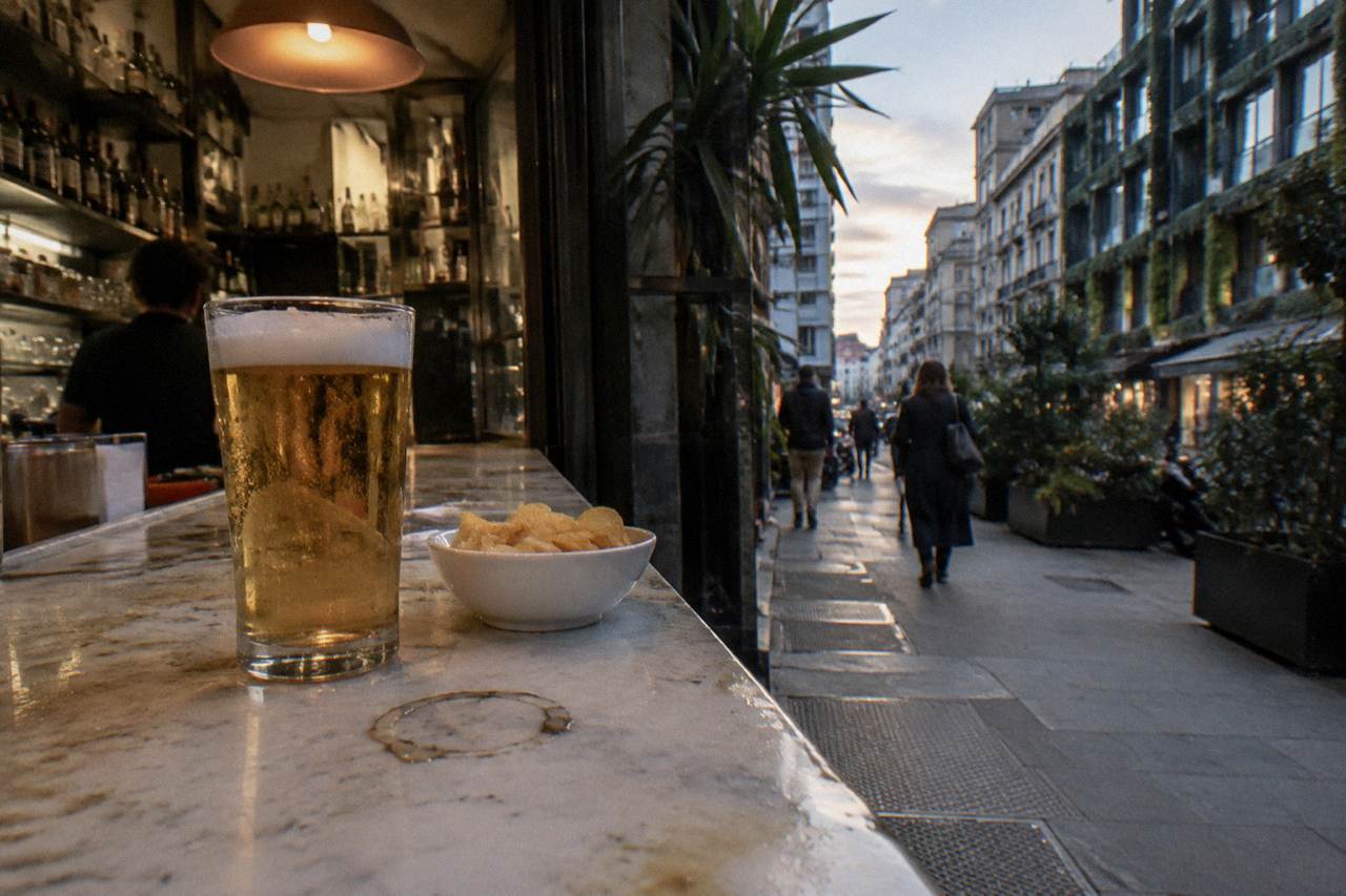 A glass of golden beer beside a small bowl of snacks on a marble bar counter
