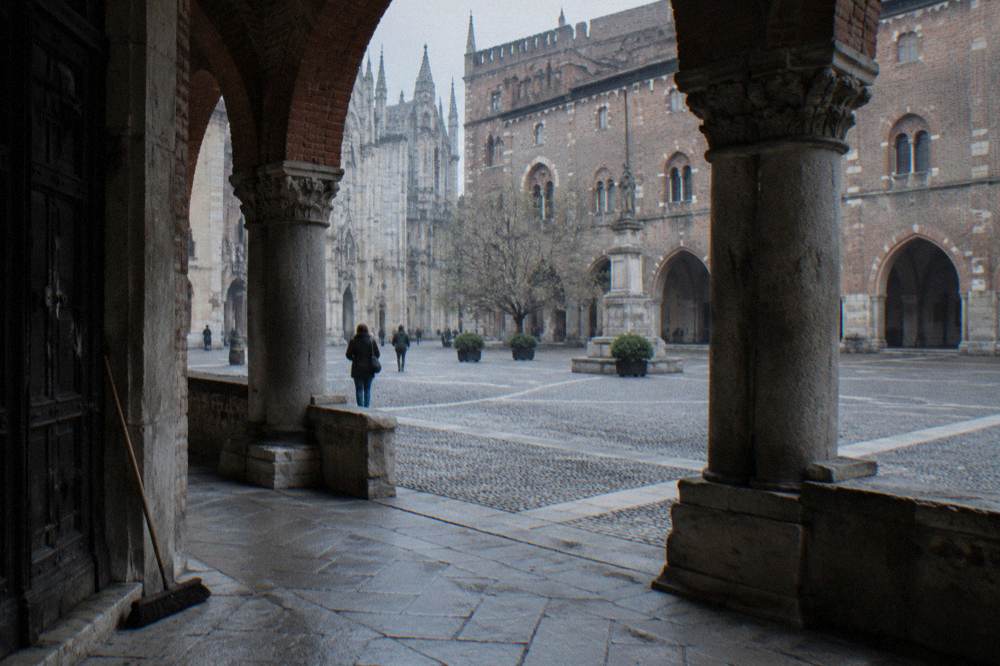 Small medieval square enclosed by brick and stone buildings with an open loggia