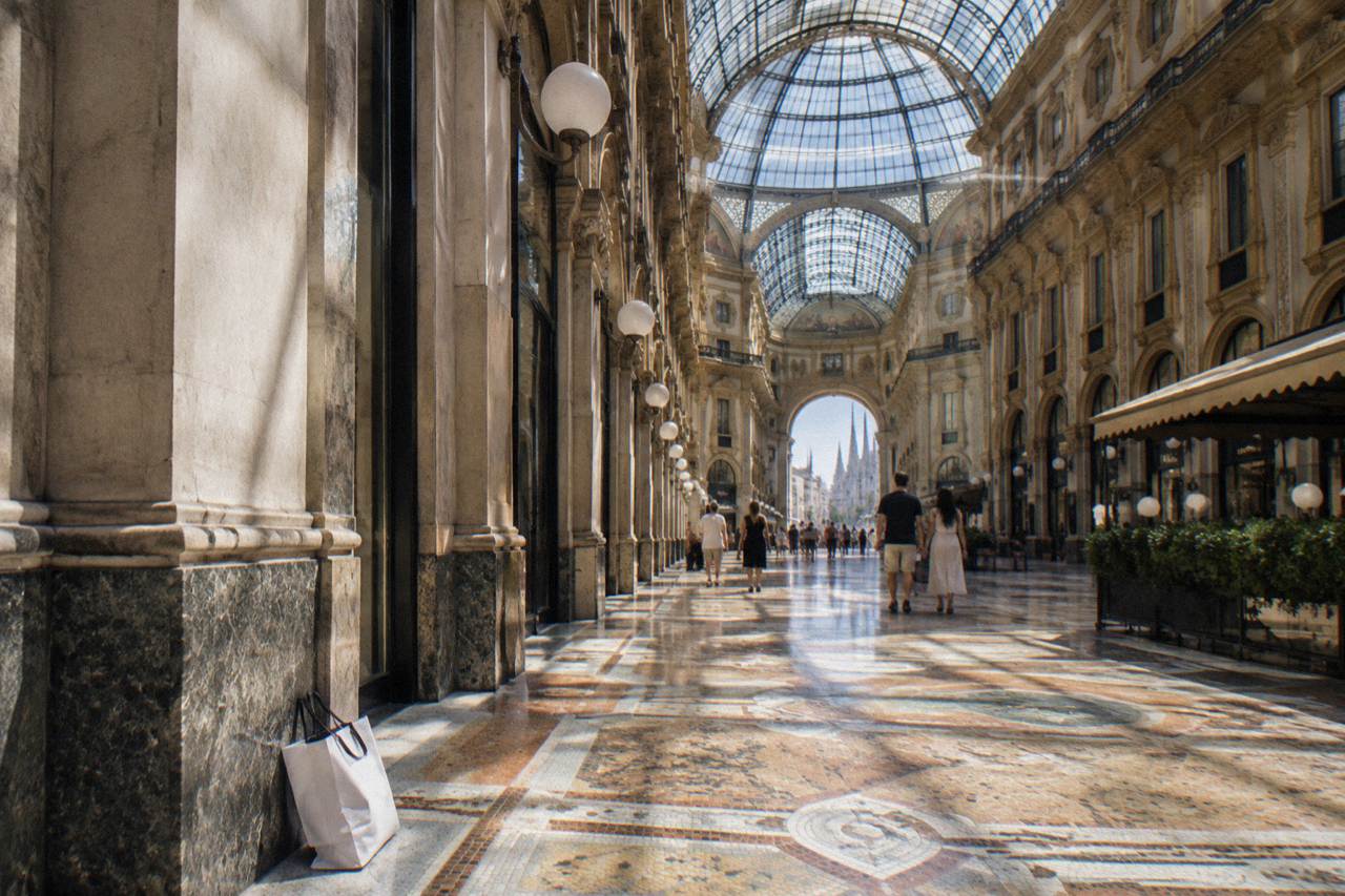 Ornate glass-vaulted shopping arcade with mosaic floor and marble facades under daylight