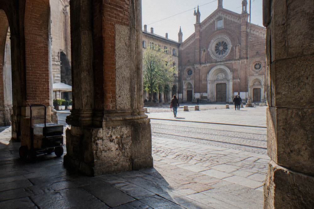 Milan street with tram tracks and stone buildings leading toward a church facade