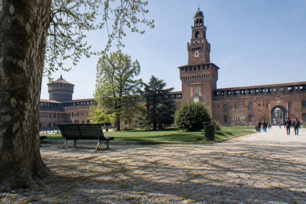 Sforza Castle courtyard with the Filarete tower and passing visitors under a clear sky
