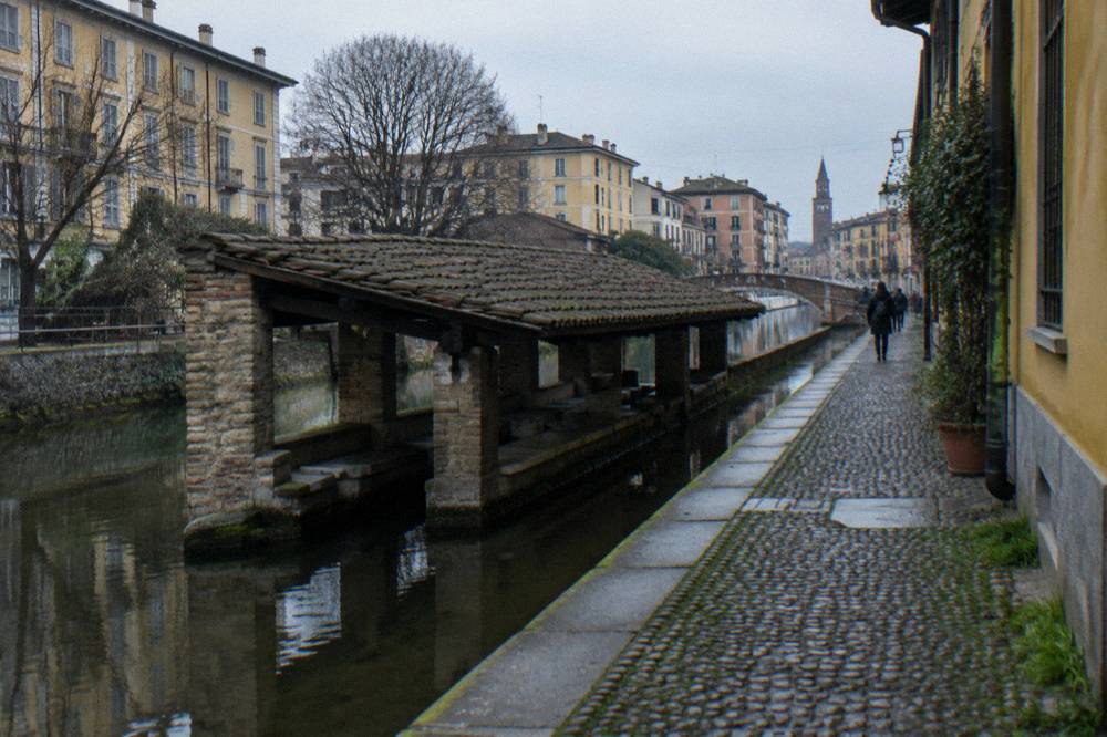 A narrow canal-side lane with old brick buildings and small shops along the water