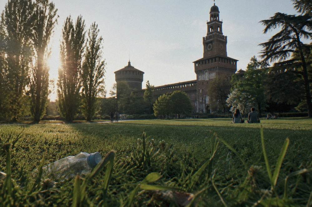 Rear facade and towers of a large brick castle seen across a green park lawn at golden hour