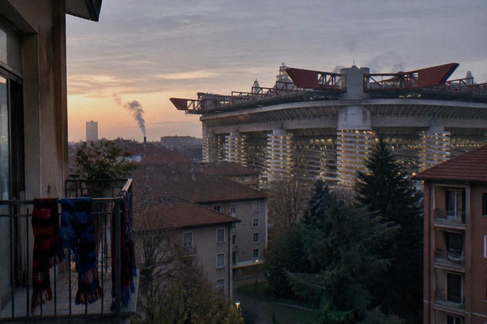 Evening view of the illuminated San Siro stadium towers above the surrounding neighbourhood rooftops