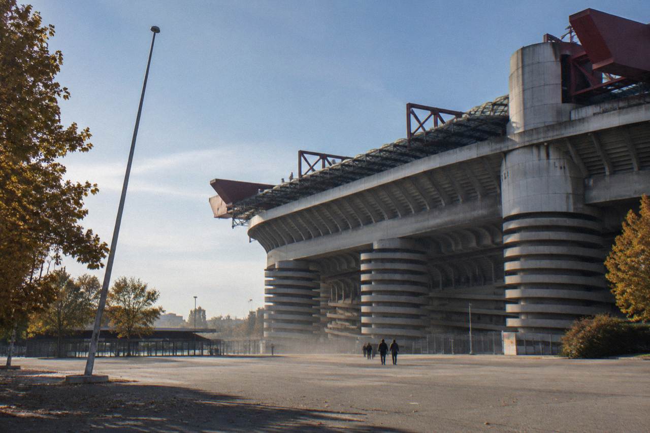 The curved exterior tiers of the San Siro stadium rising above surrounding streets under a clear sky