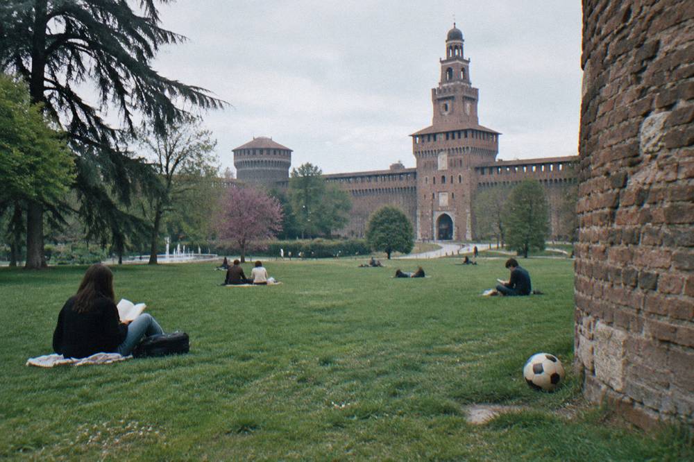 Castle stone walls and arched gateway seen from the green lawns of Parco Sempione