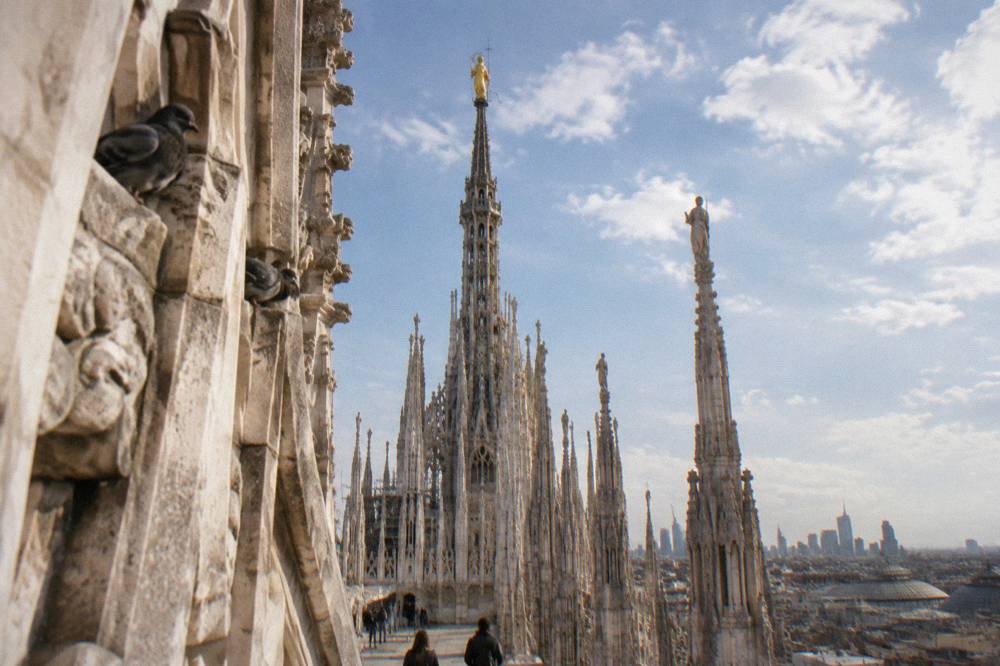 Central marble spire of Milan Cathedral rooftop with the golden Madonnina statue against the sky