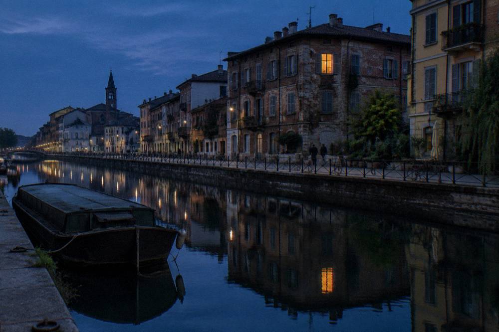 Canal-side street in Milan with old brick buildings reflected in the water at dusk