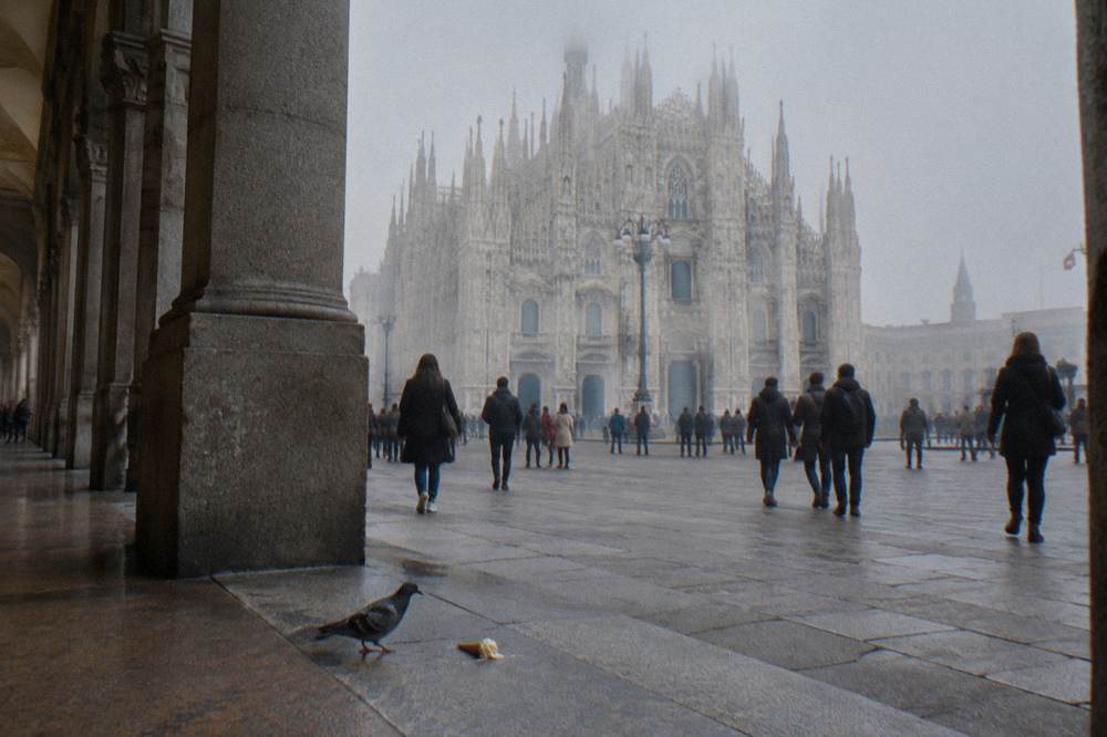 Wide city square in Milan with a grand marble cathedral facade and crowds of visitors