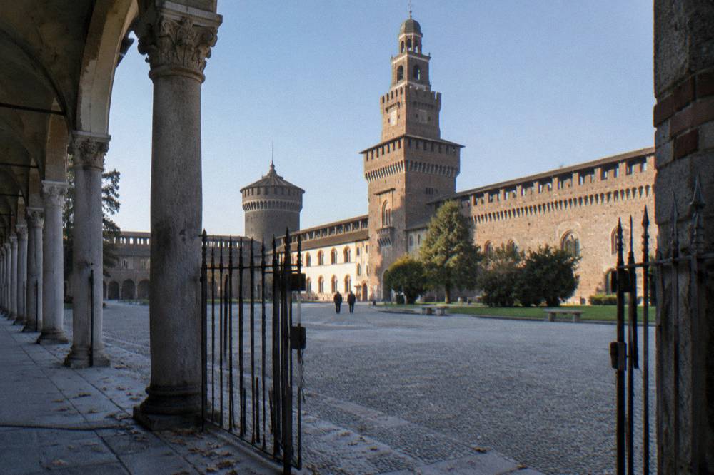 Stone fortress courtyard with tall brick towers and arched walkways under a clear sky