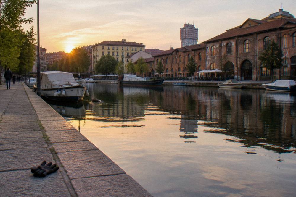 Canal-side street with old brick buildings reflected in slow water along a stone embankment