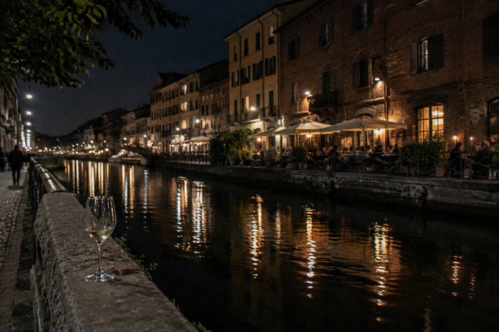The Naviglio Grande canal in Milan at dusk with lit shopfronts reflected in the water