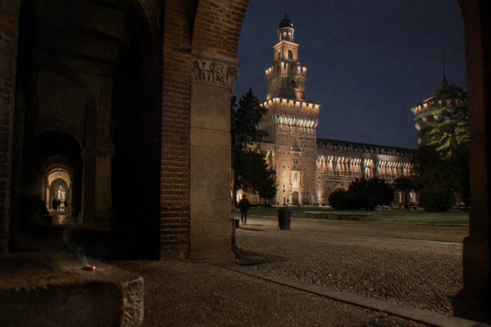 The Castello Sforzesco courtyard lit by floodlights with the tower visible beyond the arch