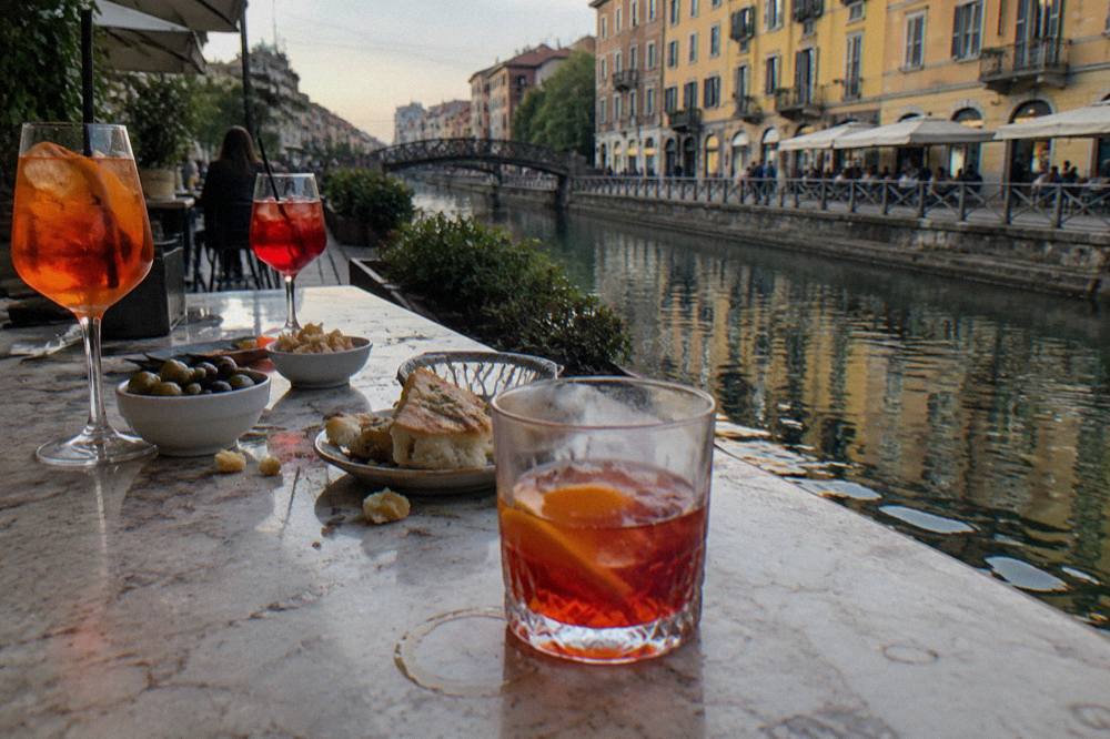 Bar counter with glasses of red and orange aperitivo drinks and small dishes of olives and focaccia