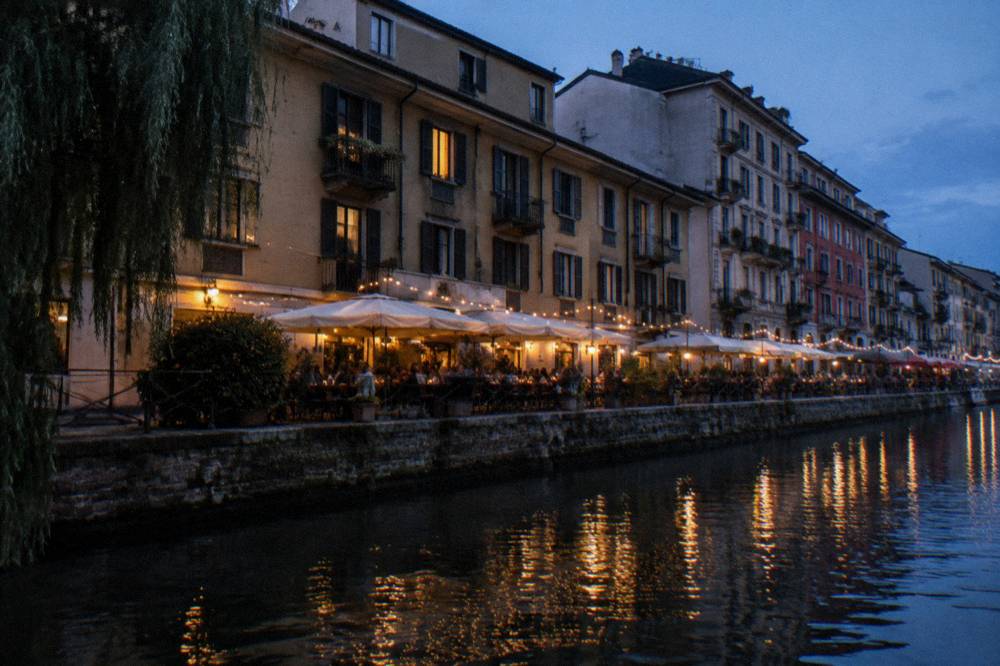 Canal-side terrace at dusk with string lights and rows of small tables