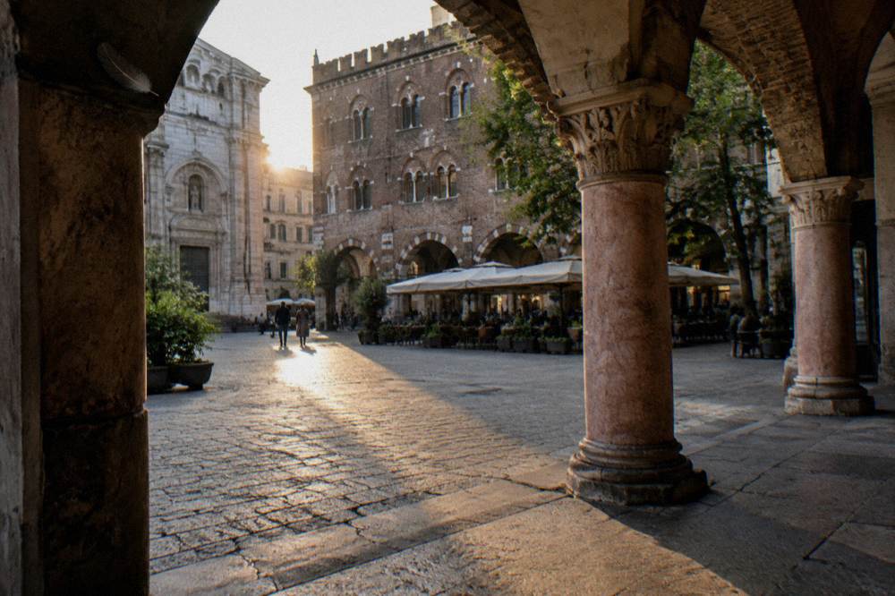 Cobblestone square at golden hour with a historic loggia building and café awnings