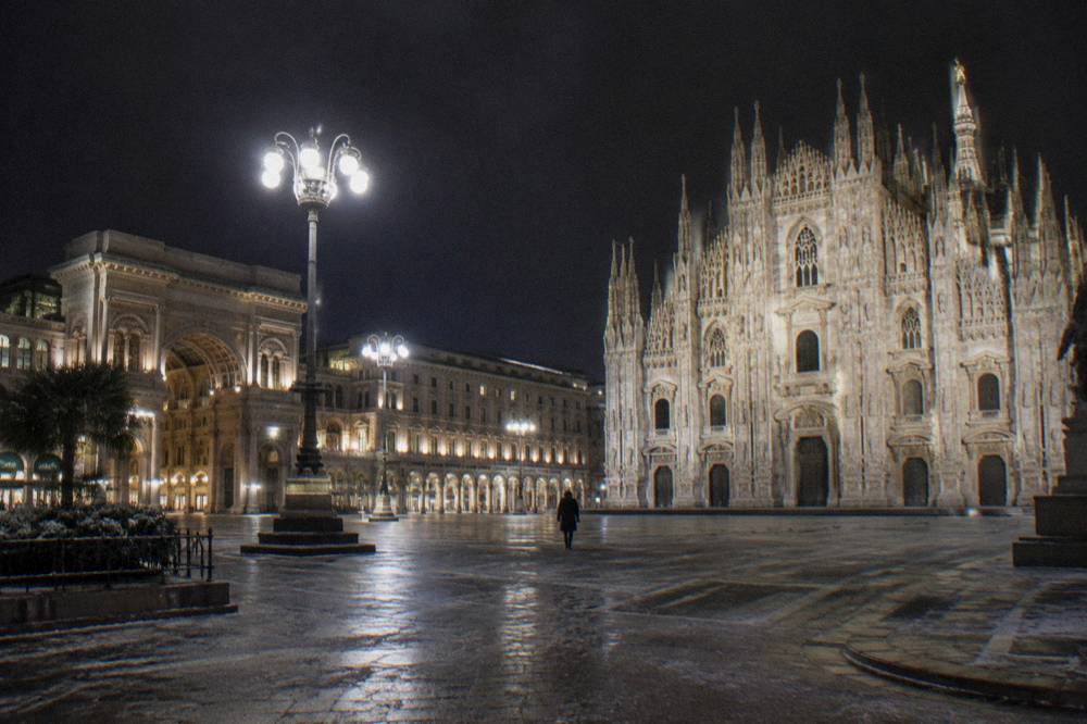 Milan cathedral facade illuminated at night above an empty square