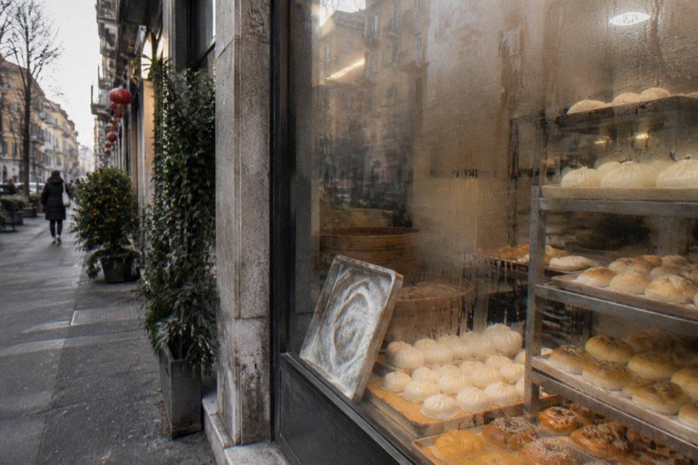 Chinese bakery window display with trays of steamed buns and pastries on Via Paolo Sarpi.