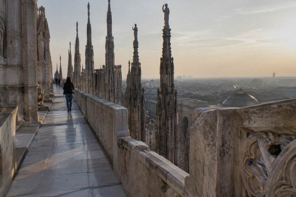 Milan cathedral rooftop walkway with marble spires and city view