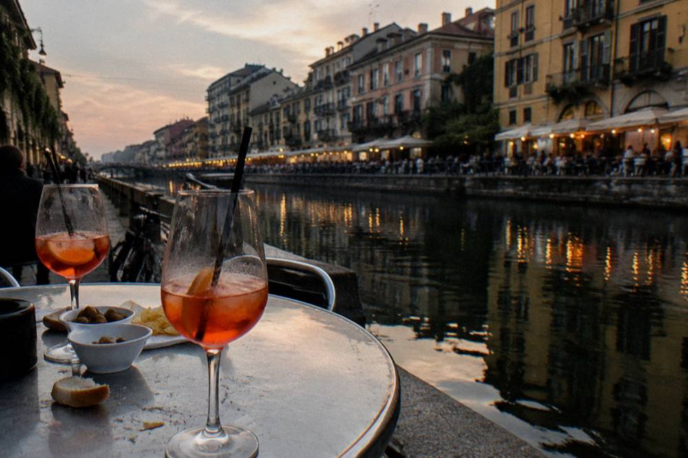 Canal-side bar tables with drinks and evening lights along the Navigli waterway