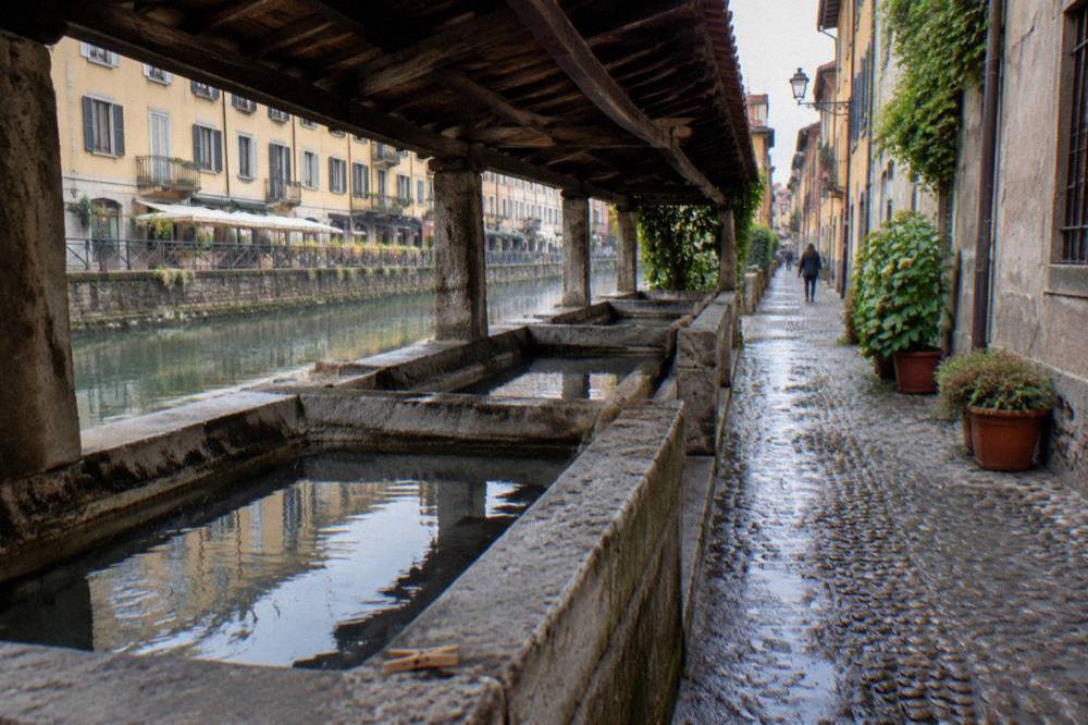 Narrow stone alley beside a Milan canal with old washing shelters