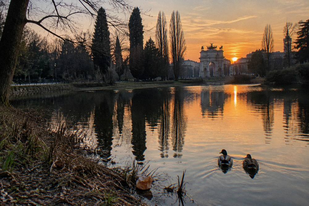 Sunset over the Parco Sempione lake with the park's trees reflected in the water