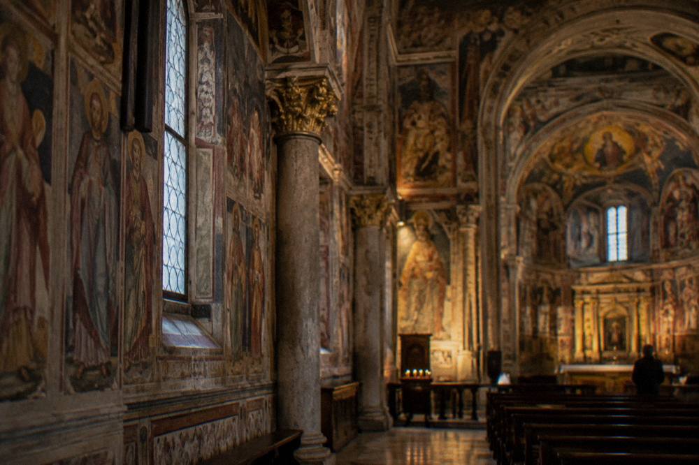 An ornate baroque church interior with frescoed walls, gilded details and soft light falling on stone columns