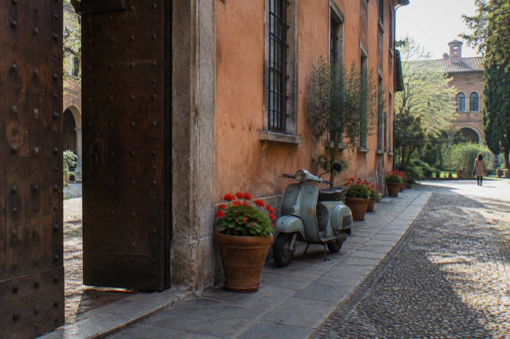 A quiet Milan street with terracotta buildings, a wooden courtyard door and potted plants along the pavement