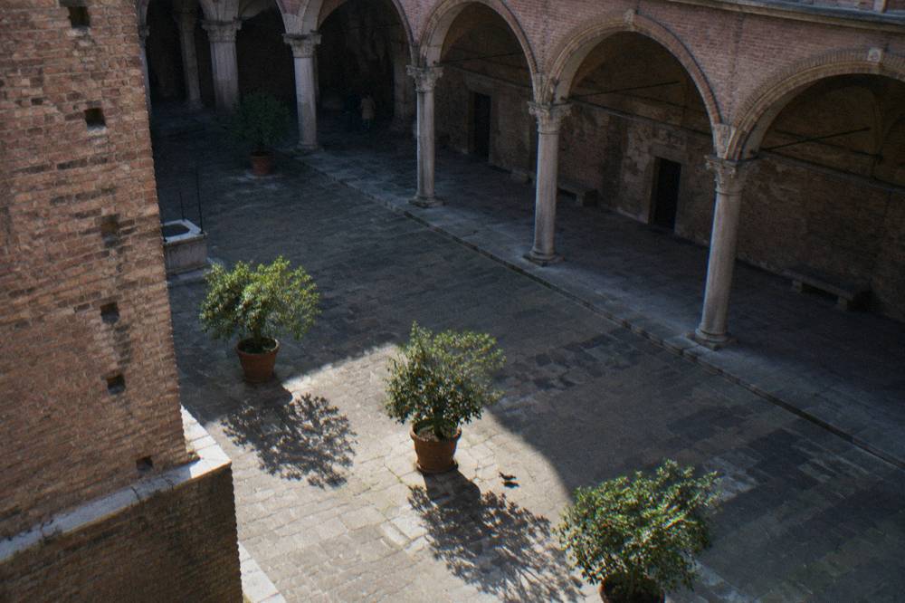A shaded Milan courtyard with arched stone loggias, potted orange trees and sunlight on worn flagstones